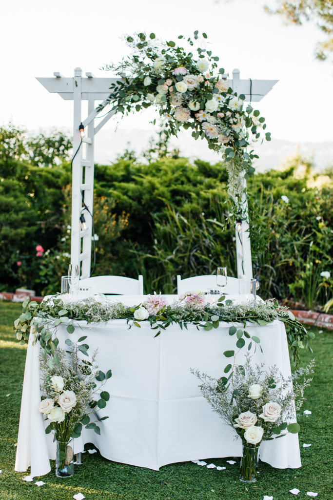 sweetheart table covered in loose greenery and blush pink florals for backyard wedding in los angeles