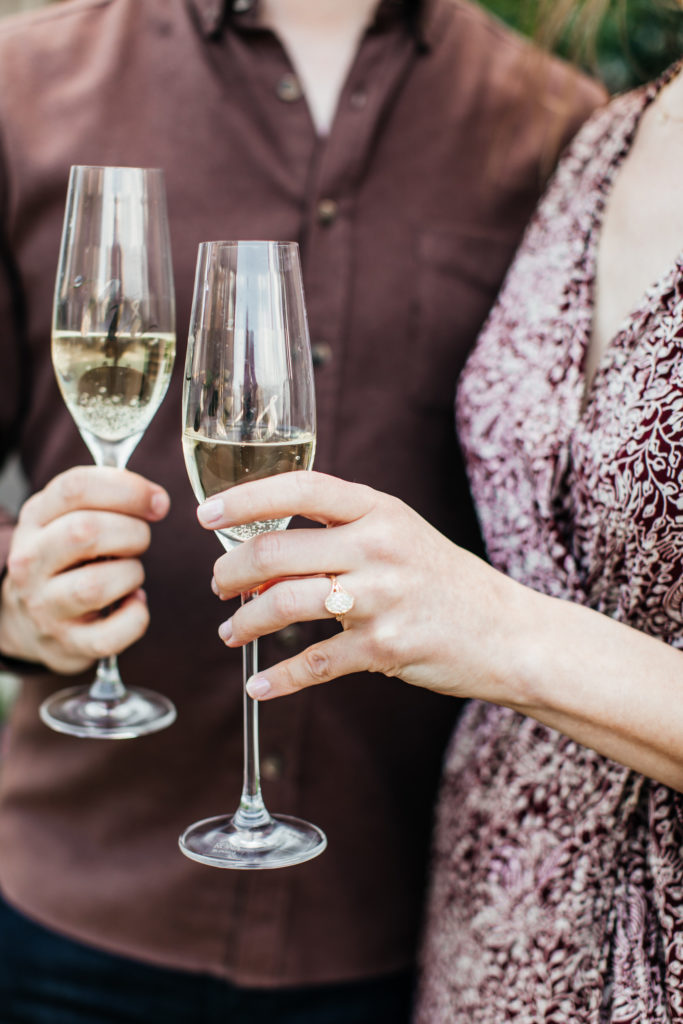 newly engaged couple holds glasses of champagne for a cheers