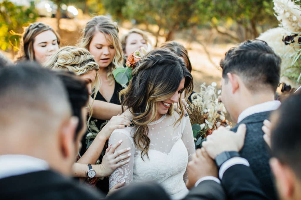 bride and groom hold hands during ceremony while bridesmaids and groomsmen pray for them