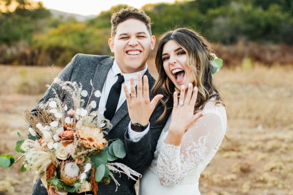 bride and groom hold up their new rings for a photo