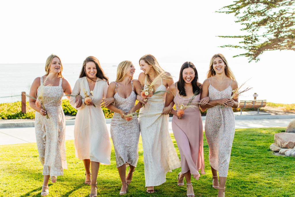 bride and bridesmaids smile and laugh for a photo while holding dried flower bouquets
