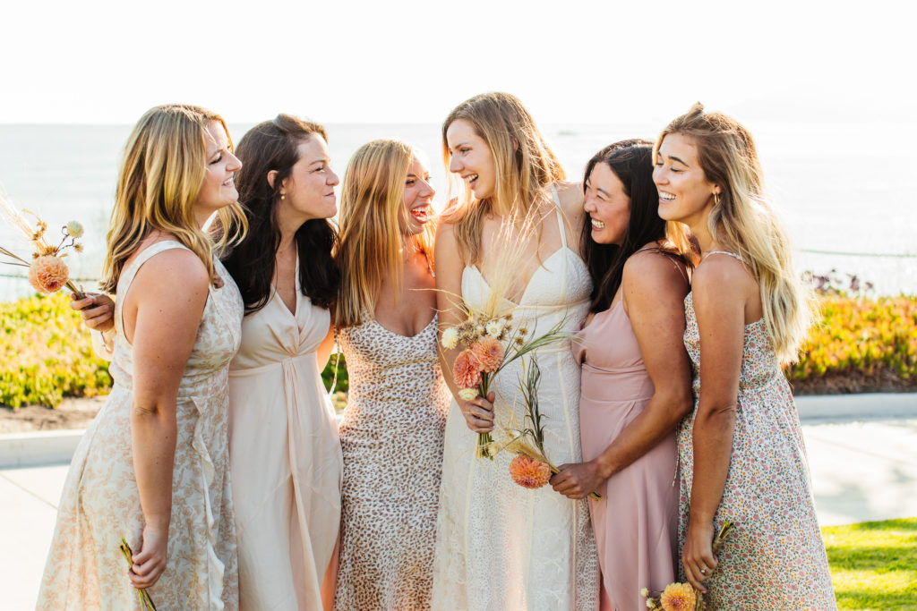 bridesmaids smile and laugh for a candid photo, bridesmaids wear neutral patterned dresses 