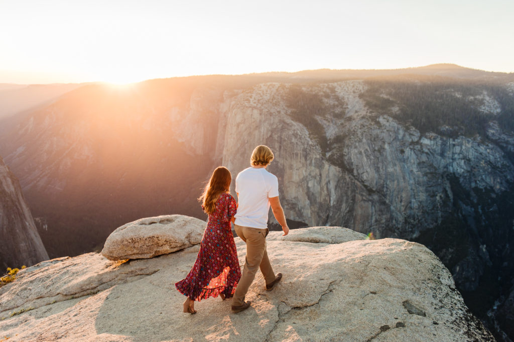 taft point engagement photos in Yosemite couple holds hands and walks towards the sunset
