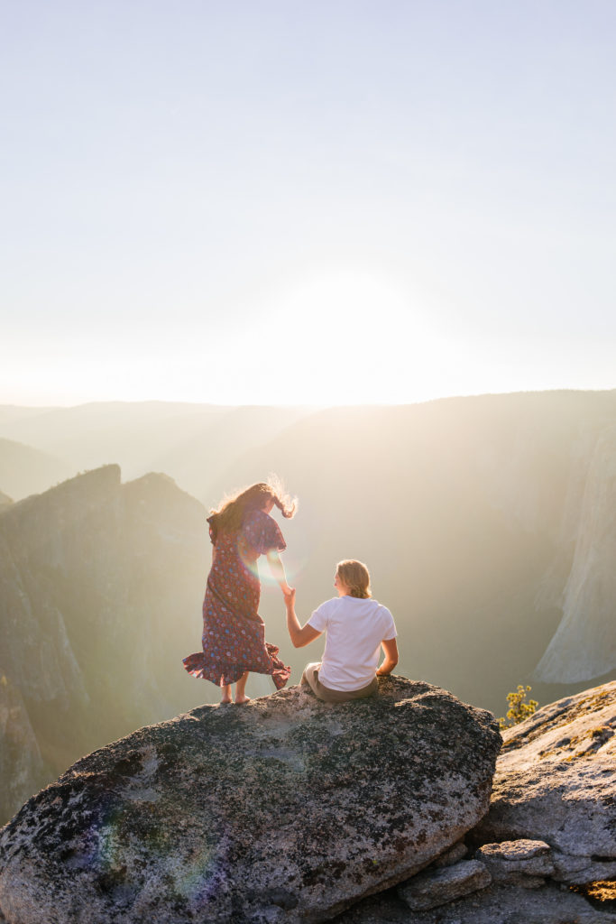 groom helps bride down onto a ledge at Yosemite national park engagement