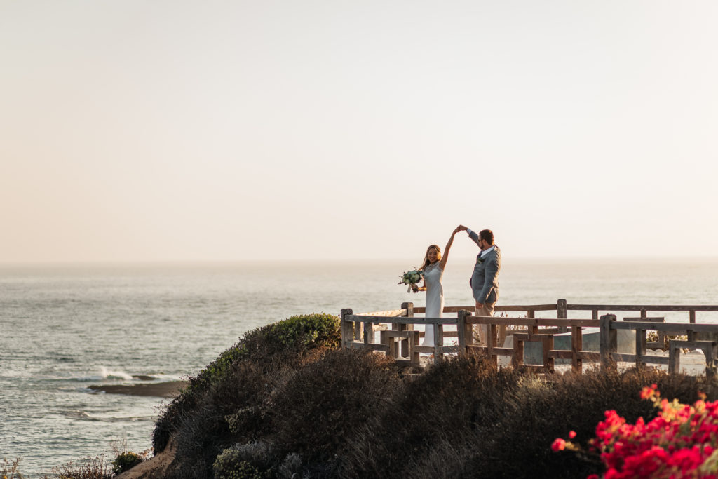 bride and groom dance on a cliff by the ocean together