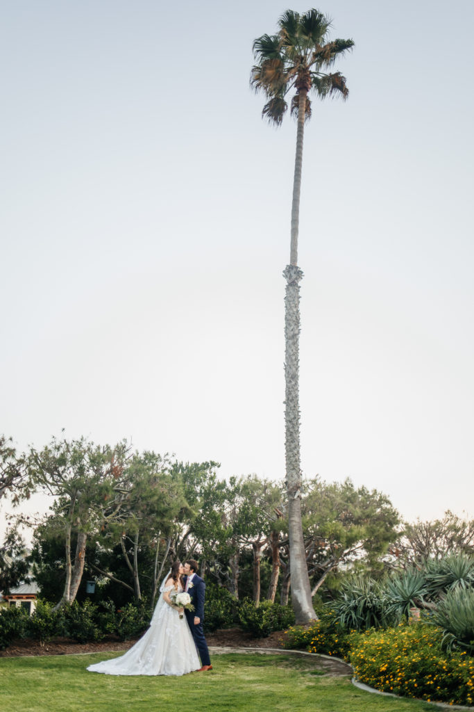 bride and groom kiss under a palm tree in Newport Beach