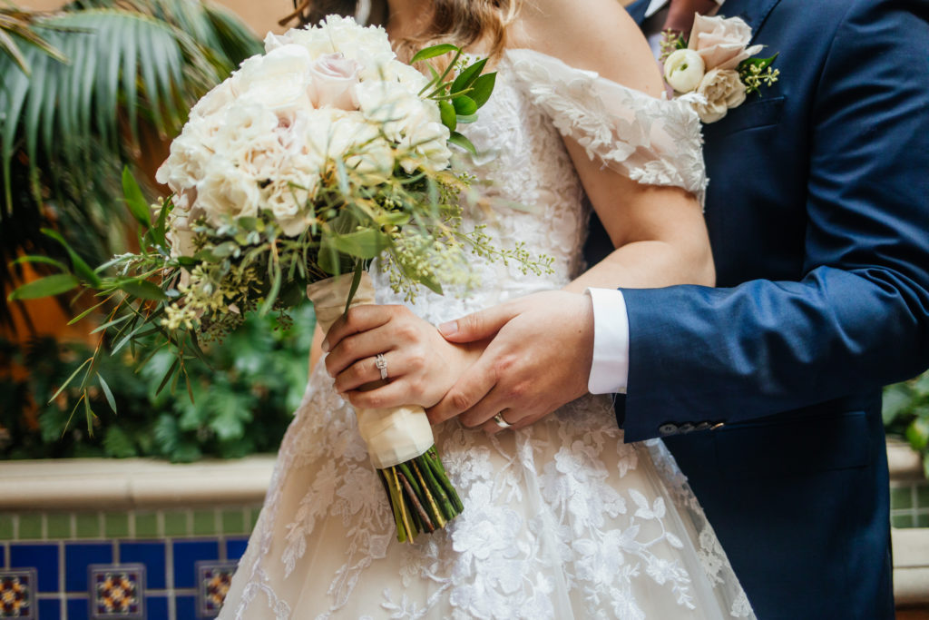 detail photo of bride and grooms hands and rings on bouquet