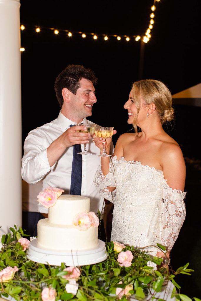bride and groom smile at each other and cheers with champagne after their cake cutting
