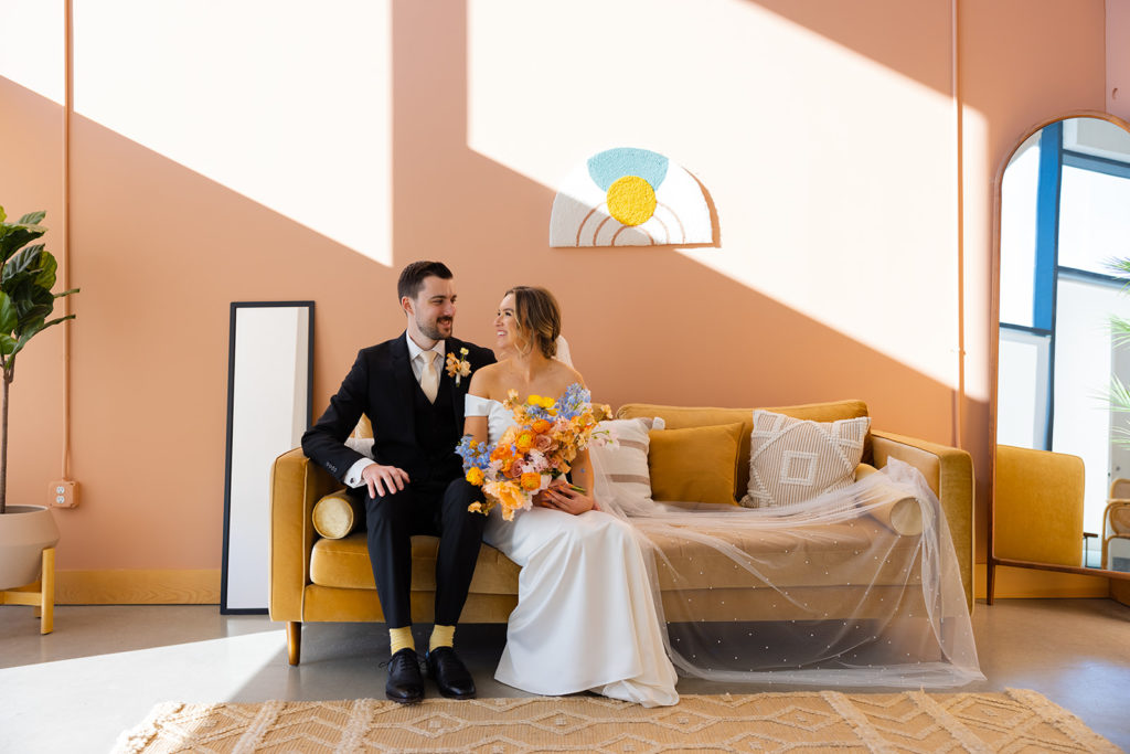 bride and groom sitting on a couch at their colorful wedding venue