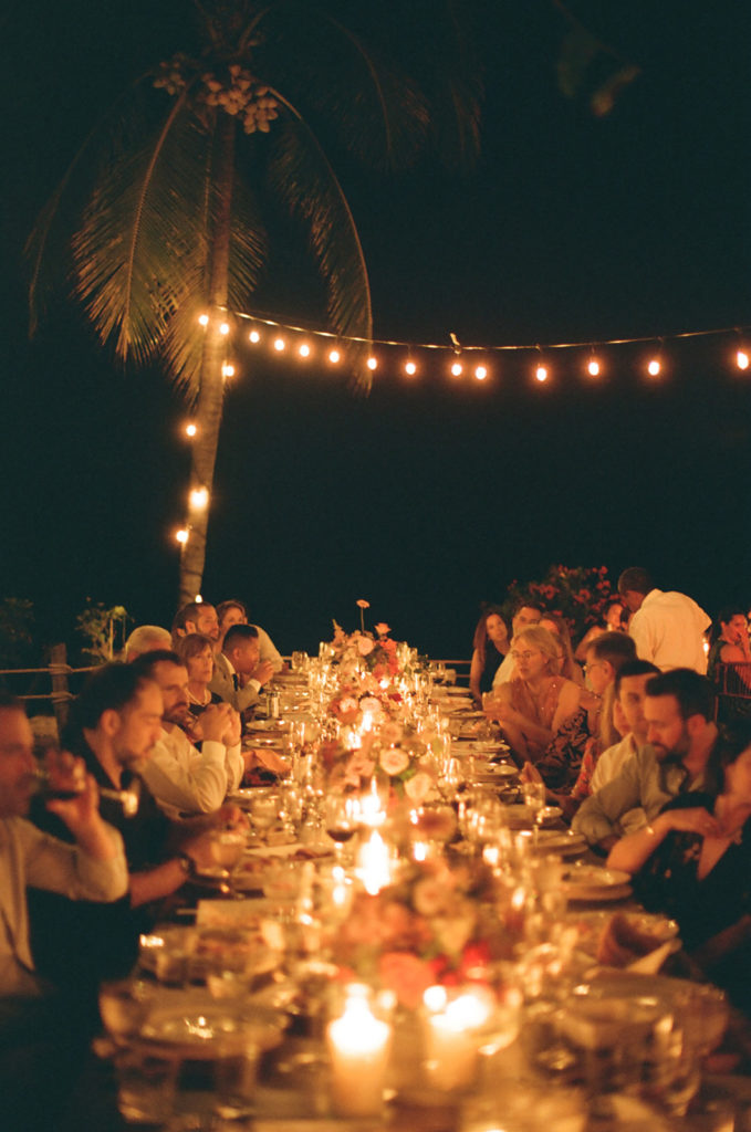 wedding guests enjoy dinner at a long table under string lights