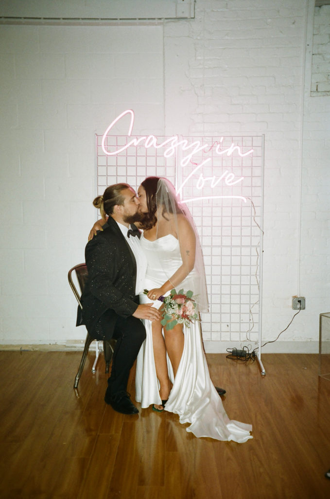 bride and groom kiss under neon sign