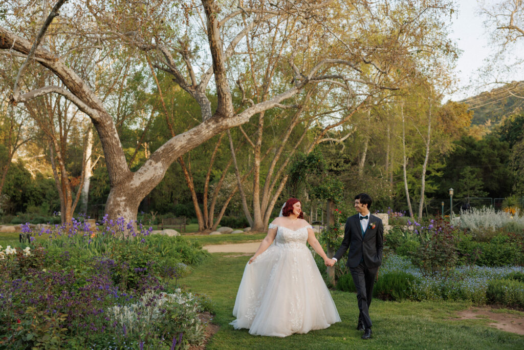 bride and groom walk hand in hand through a garden together on their wedding day