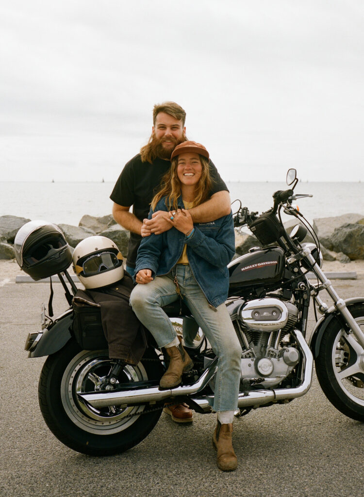 couple smiles at the camera while sitting on their motorcycle