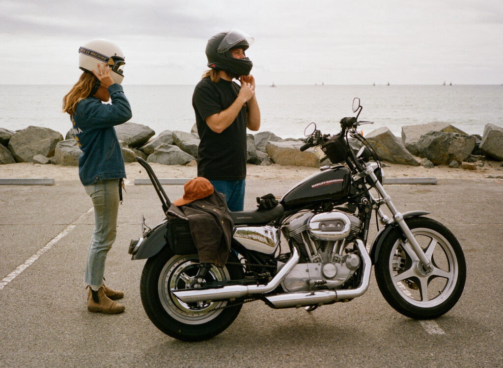 couple puts on helmets for their motorcycle engagement photos in San Clemente