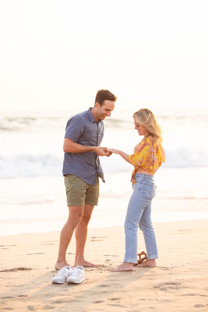man places ring on his girlfriend's finger during a romantic proposal on the beach in Los Angeles