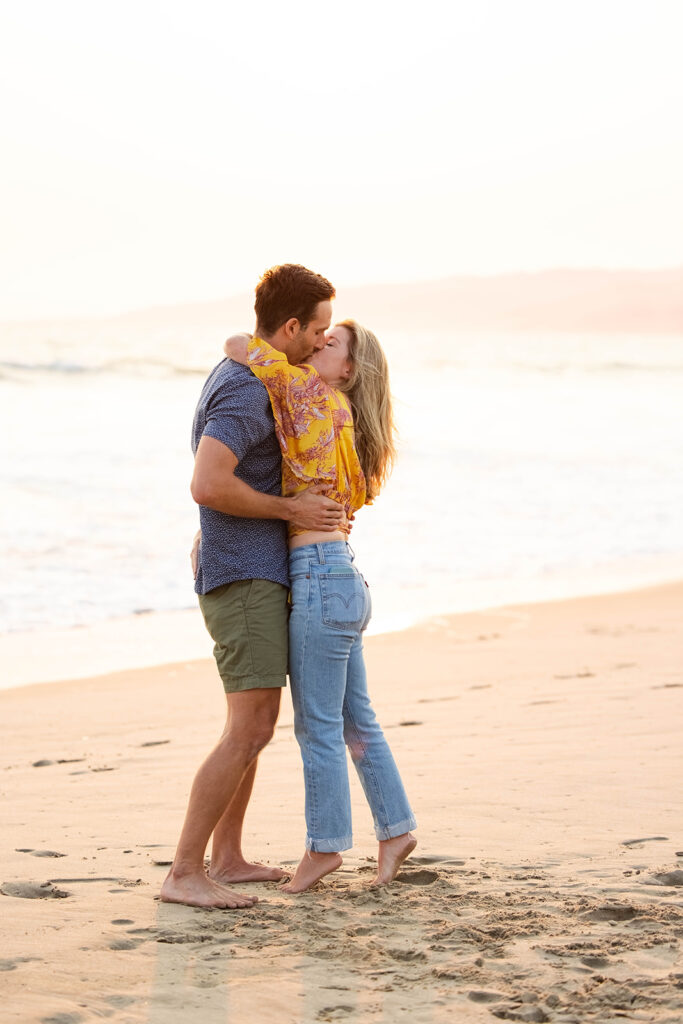 couple kisses after their beach proposal at sunset