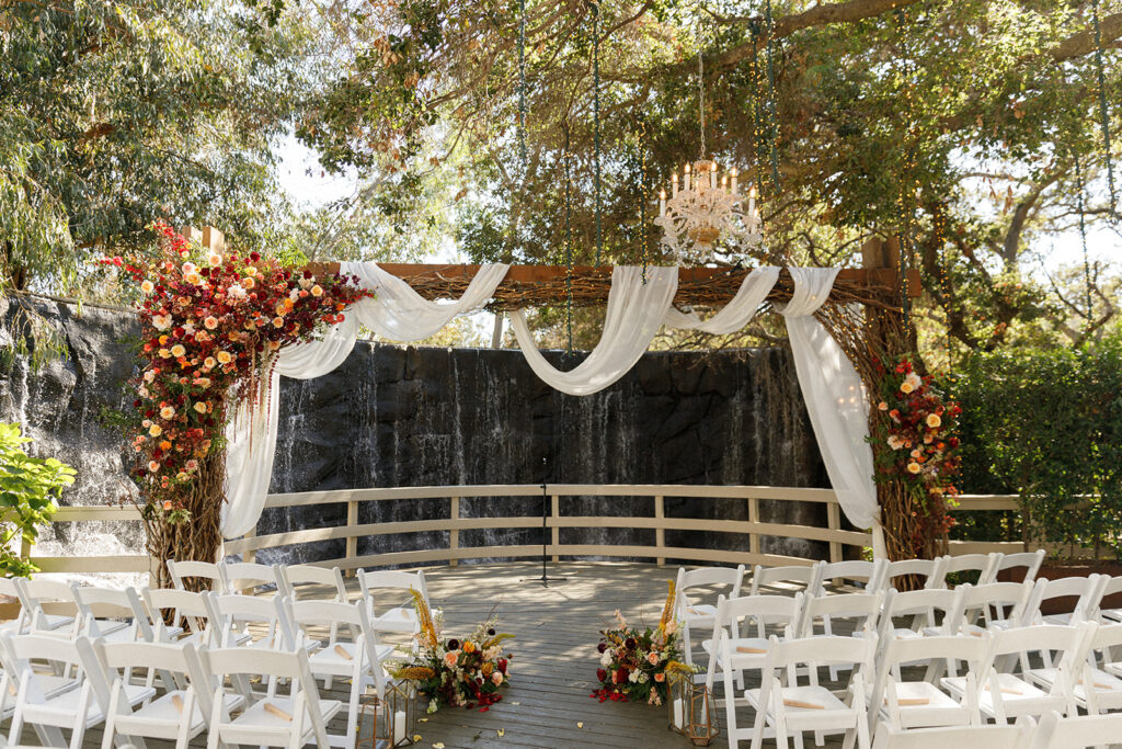 jewel-toned floral wedding arch decorated with drapery, twinkle lights, and twisted branches for a fairytale aesthetic