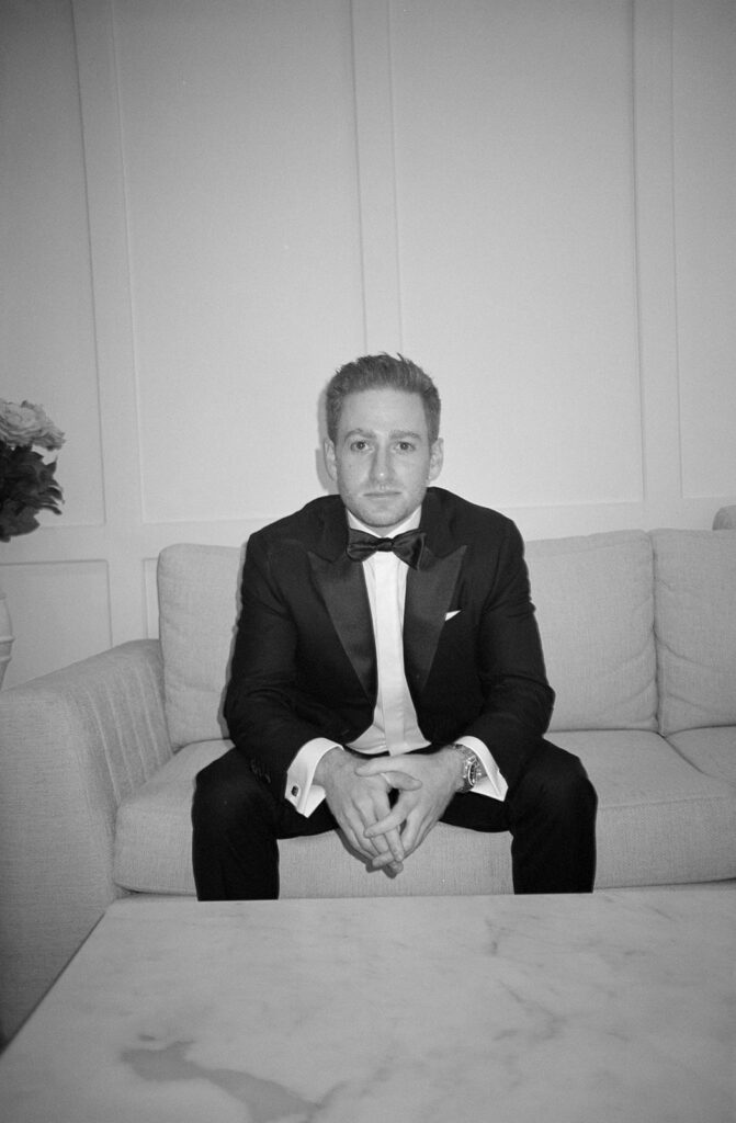 groom sits on the couch to pose for a portrait inside the getting ready room at Birchwood Room wedding venue