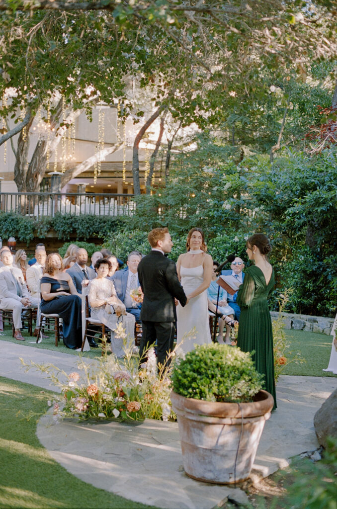 side view of bride and groom holding hands in front of their guests at a wedding ceremony at Birchwood Room